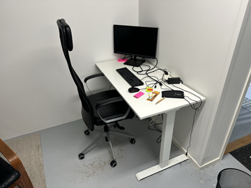 Höj- och sänkbart skrivbord med kontorsstol, datorskärm, tangentbord och datormus